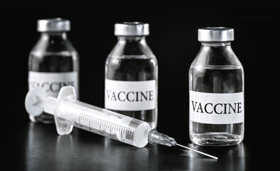 Three glass vaccine vials on black board, hypodermic syringe near
