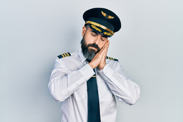 Young hispanic man wearing airplane pilot uniform sleeping tired dreaming and posing with hands...