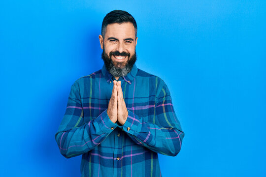 Young hispanic man wearing casual clothes praying with hands together asking for forgiveness smiling confident.