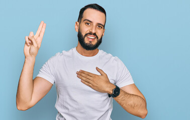 Young man with beard wearing casual white t shirt smiling swearing with hand on chest and fingers...