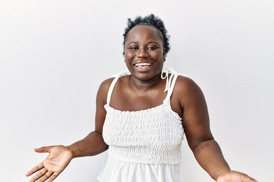 Young african woman standing over white isolated background smiling cheerful with open arms as friendly welcome, positive and confident greetings