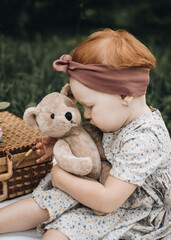 Sweet little girl is hugging a teddy bear, while sitting at the summer garden. Child is playing with toy. Vintage picnic.