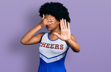 Young african american woman wearing cheerleader uniform covering eyes with hands and doing stop...