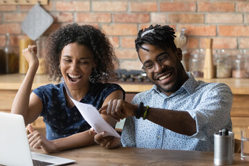 Happy excited young Black couple celebrating financial success, achieve, holding papers, reading...