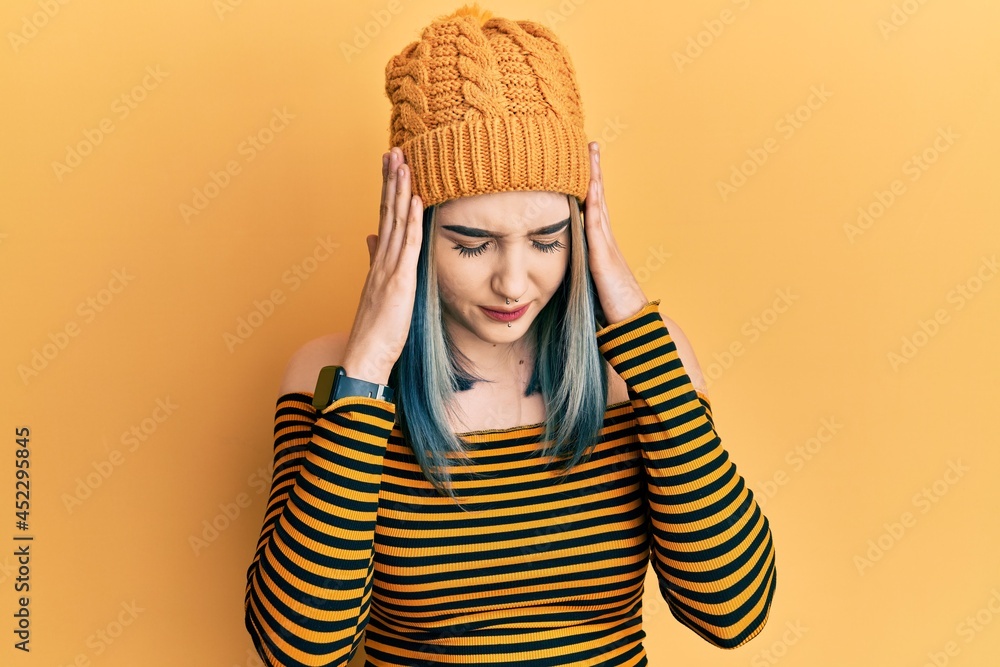 Sticker Young modern girl wearing wool hat with hand on head for pain in head because stress. suffering migraine.