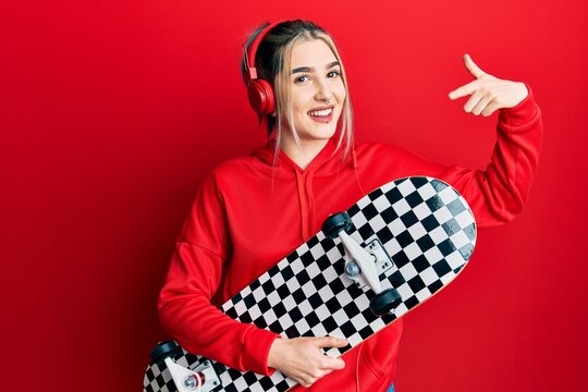Young modern girl holding skate wearing headphones smiling happy pointing with hand and finger