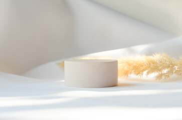Round plaster podium for advertising cosmetic products on a delicate light background with a sprig of pompous herbs.
