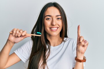 Young hispanic girl holding toothbrush with toothpaste smiling with an idea or question pointing finger with happy face, number one