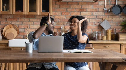 Happy successful Afro American couple celebrating financial achieve at laptop, giving high five....