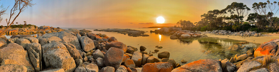 Panorama of sunrise over the ocean at Bay of Fires. Orange lichen covered rocks. Tasmania, Australia. No people, copy space.
