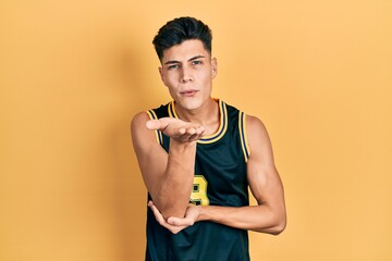 Young hispanic man wearing basketball uniform looking at the camera blowing a kiss with hand on air...