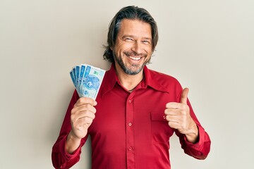 Middle age handsome man holding 50 polish zloty banknotes smiling happy and positive, thumb up doing excellent and approval sign