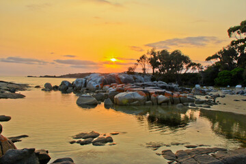 Sunrise over ocean inlet lined with rocks covered with orange lichen. Bay of Fires Tasmania, Australia. No people. Copy Space