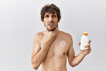 Fototapeta premium Young hispanic man standing shirtless holding sunscreen lotion touching painful neck, sore throat for flu, clod and infection