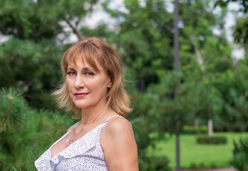 Naklejka premium blonde woman, 50 years old portrait close-up against the background of a green park