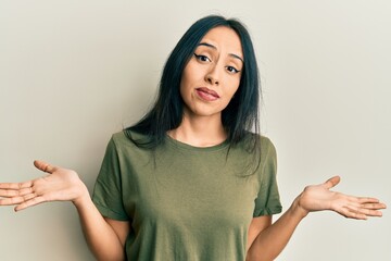 Young hispanic girl wearing casual t shirt clueless and confused expression with arms and hands...