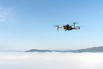 Fototapeta na wymiar flying a quadrocopter helicopter drone in the air, in a clear blue sky, morning fog and mountains below. aerial photo and video shooting using gadgets and modern devices. modern technologies allow you