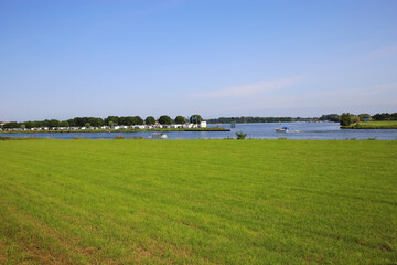 Roermond (Marina Resort Oolderhuuske), July 9. 2021: View over green meadow and river Maas on island with campsite against blue summer sky