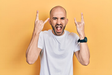 Fototapeta premium Young bald man wearing casual white t shirt shouting with crazy expression doing rock symbol with hands up. music star. heavy music concept.
