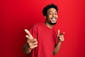 Young african american man with beard wearing casual red t shirt pointing fingers to camera with happy and funny face. good energy and vibes.