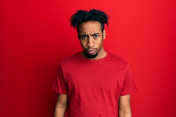 Fototapeta na wymiar Young african american man with beard wearing casual red t shirt skeptic and nervous, frowning upset because of problem. negative person.