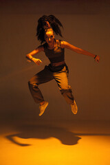Dancing mixed race girl jumping and levitating in warm studio light. Female dancer performer jump in hip hop dance