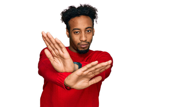 Young african american man with beard wearing casual winter sweater rejection expression crossing arms and palms doing negative sign, angry face