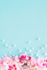 Creative blue background with pink blooming flowers and .pearls. Minimal flat lay concept with copy space.