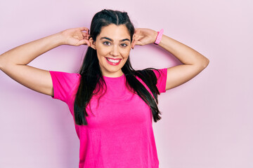 Young hispanic girl wearing casual pink t shirt smiling pulling ears with fingers, funny gesture. audition problem