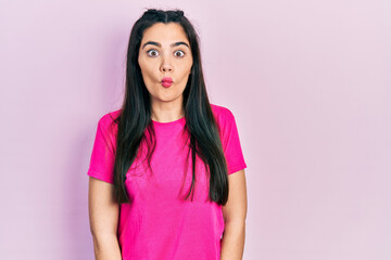 Fototapeta premium Young hispanic girl wearing casual pink t shirt making fish face with lips, crazy and comical gesture. funny expression.