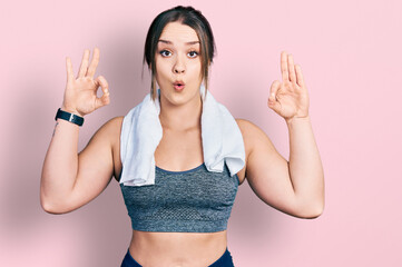 Young hispanic girl wearing sportswear and towel looking surprised and shocked doing ok approval symbol with fingers. crazy expression