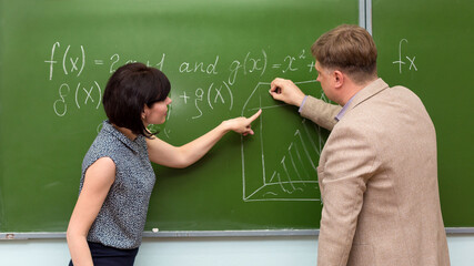 A student at the blackboard at the institute at the department passes an exam in mathematics to the teacher actively explaining her solution to the problem.