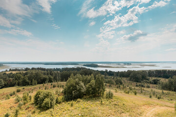 Fototapeta premium Summer nature landscape with sky, clouds, grass, forest trees and water lakes in the bottom. Rural scenery. Natural scene.