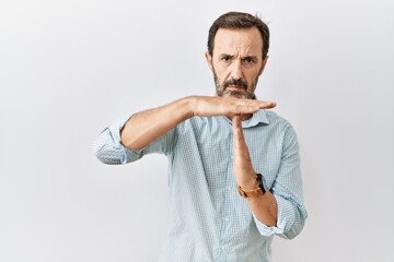 Middle age hispanic man with beard standing over isolated background doing time out gesture with hands, frustrated and serious face