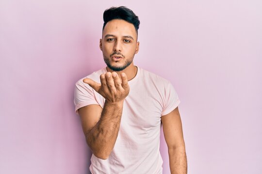 Young arab man wearing casual clothes looking at the camera blowing a kiss with hand on air being lovely and sexy. love expression.