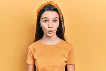 Young brunette girl wearing casual orange t shirt scared and amazed with open mouth for surprise,...