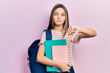 Young brunette girl holding student backpack and books with angry face, negative sign showing...