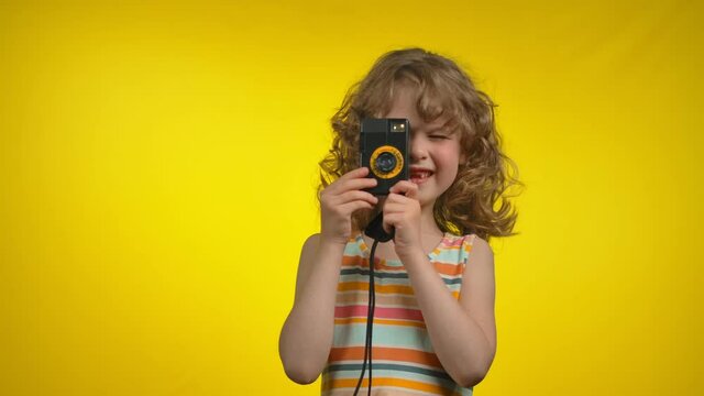 Girl is using retro photo camera for shooting pictures in the yellow background