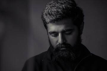 Fototapeta premium sad man boy portrait. upset person looking down. hopeless situation. black and white single light. beard indian young handsome guy. heart brake. business loss. facing failure in life.