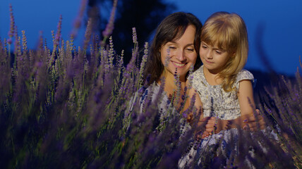 Happy young mother and little girl daughter kid kissing and laughing in aromatic flowers lavender field garden on summer night sunset. Family, childhood, motherhood, fairytale, provence style concept © Andrii Iemelianenko