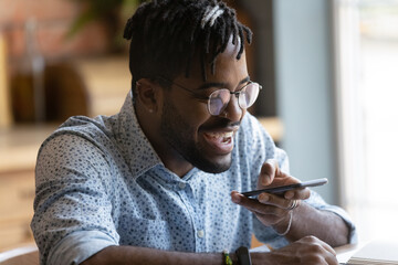 Happy millennial Black hipster guy using voice recognition app on smartphone, recording audio...