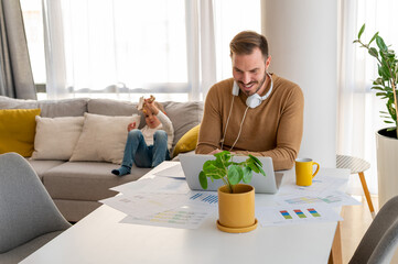 Young father working from home with child playing in the background