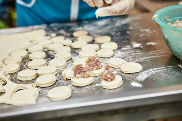 Chef hands sculpt dumplings on background of cutting boards with handmade, ravioli and khinkali sprinkled with flour on a table. Delicious homemade food.