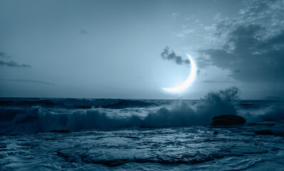Waves crashing over rocks from the ocean with amazing crescent moon