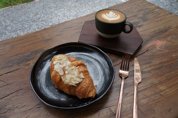 Croissant in a black plate and coffee on a wooden table