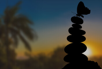 Papillon sur galets empilées sur fond de soleil couchant 