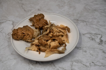 Washed wheat flour seitan shredded and ready for using in vegan recipes. White plate and white marble table.