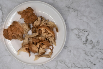 Washed wheat flour seitan shredded and ready for using in vegan recipes. White plate and white marble table.