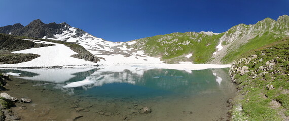 Fototapeta na wymiar Panoramique lors de la randonnée des 5 lacs du Forclaz : le lac Noir gelé partiellement