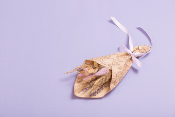 bouquet of dried flowers in craft paper on  lilac background